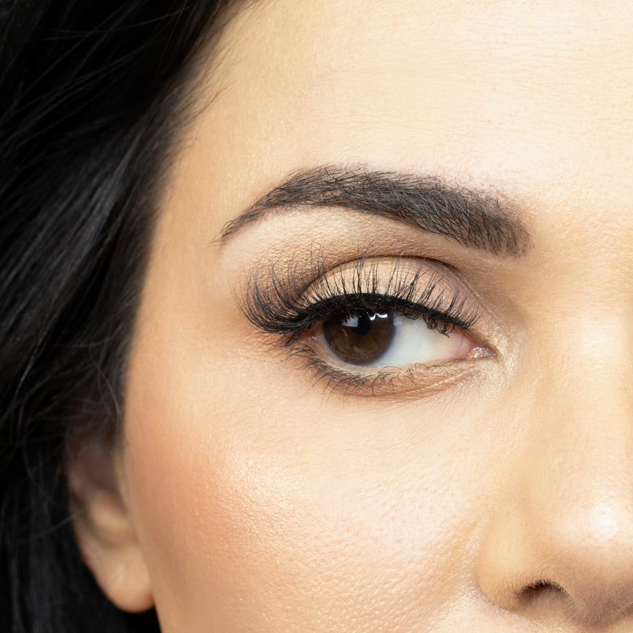 Close up of a young woman's right eye looking to the side while wearing Suntarah Beauty's Faux Mink False Strip Lash in style F-102. Lash appears very light and wispy.