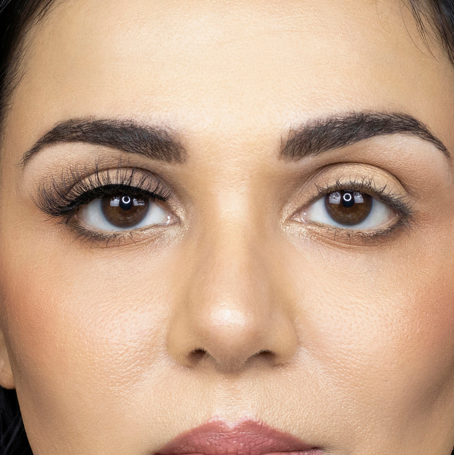 Close up of a young woman looking straight ahead while wearing Suntarah Beauty 3D Faux Mink False Strip Eyelash in style F-102 on right eye only, and no false lash on left eye. There is a subtle but appealing difference in appearance between both eyes. Right eye is accentuated while appearing natural.