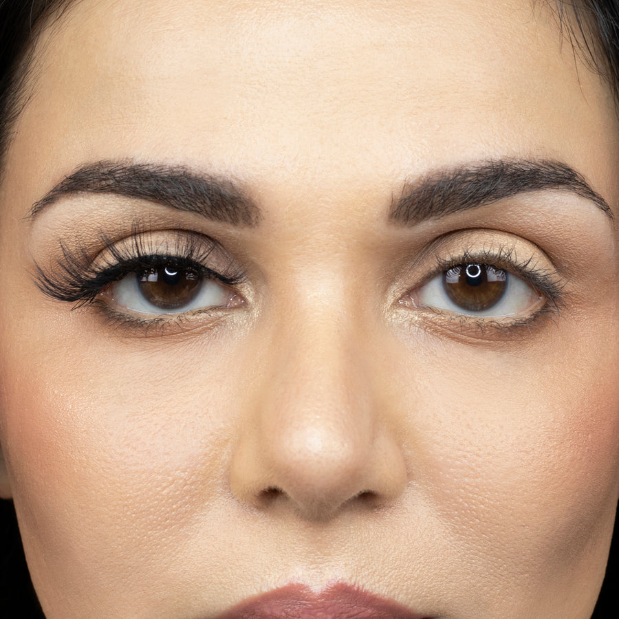 Close up of a young woman looking straight ahead and wearing Suntarah Beauty 3D Faux Mink Strip Lash in style F-103 on her right eye, and no false lash on her left eye. There is a significant difference between both eyes. Right eye is accentuated with wispy lashes and a foxy look.