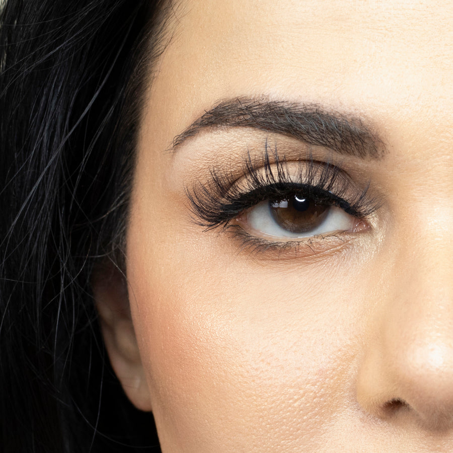 Close up of the right eye of a woman looking straight ahead and wearing Suntarah Beauty 3D Faux Mink lash in style F-104. Lash looks wispy, and curls upwards.