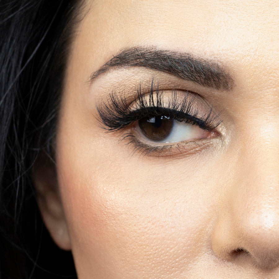  Close up of a woman's right eye looking to the side while wearing Suntarah Beauty 3D Faux Mink lash in style F-104. Lash appears lightweight, wispy, and has a significant curl.